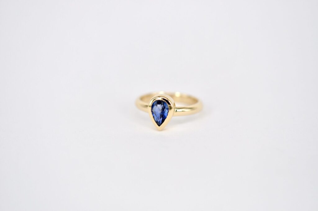 Handgefertigter Ring aus Gelbgold von Goldschmiede Stephanie Berger mit einem im Tropfenschliff gefassten, blauen Saphir.